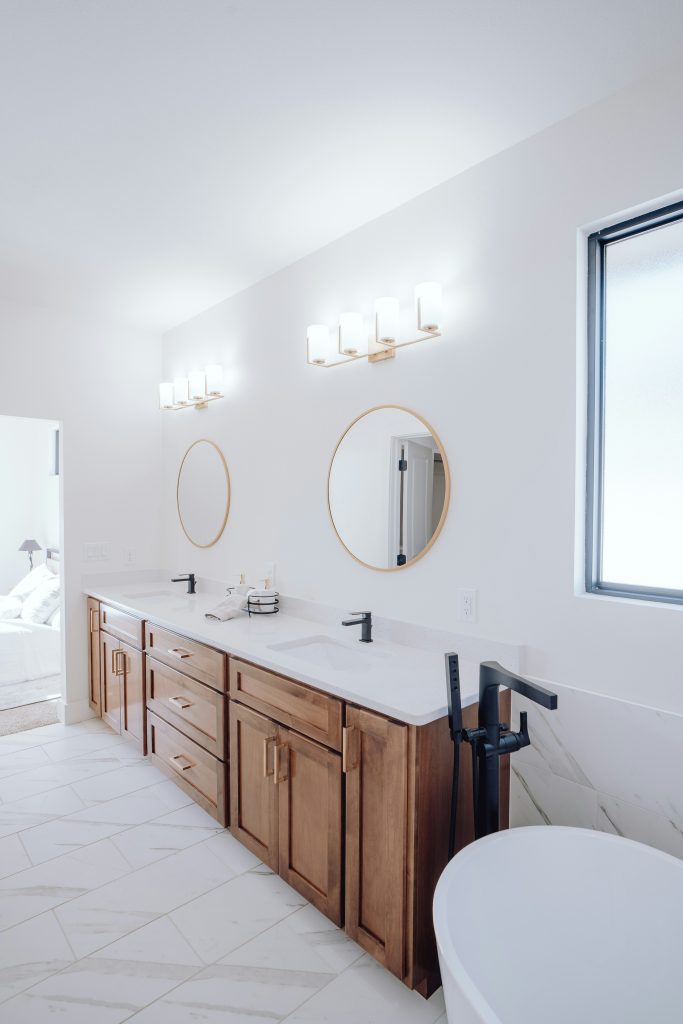 Modern bathroom featuring a wooden double vanity with quartz countertop, dual mirrors, and a freestanding bathtub with black fixtures.